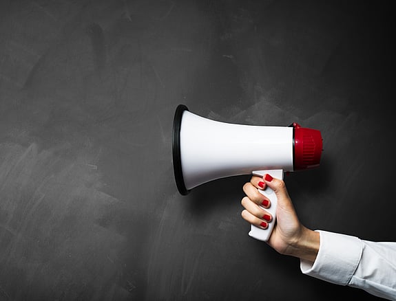 Debattartikel. En hand som håller i en megafon.