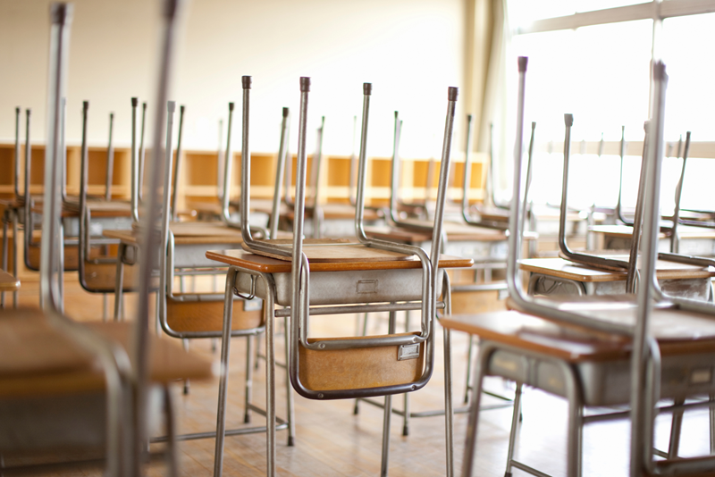 Stolar är upp och nervända på skolbänkar i tomt klassrum 