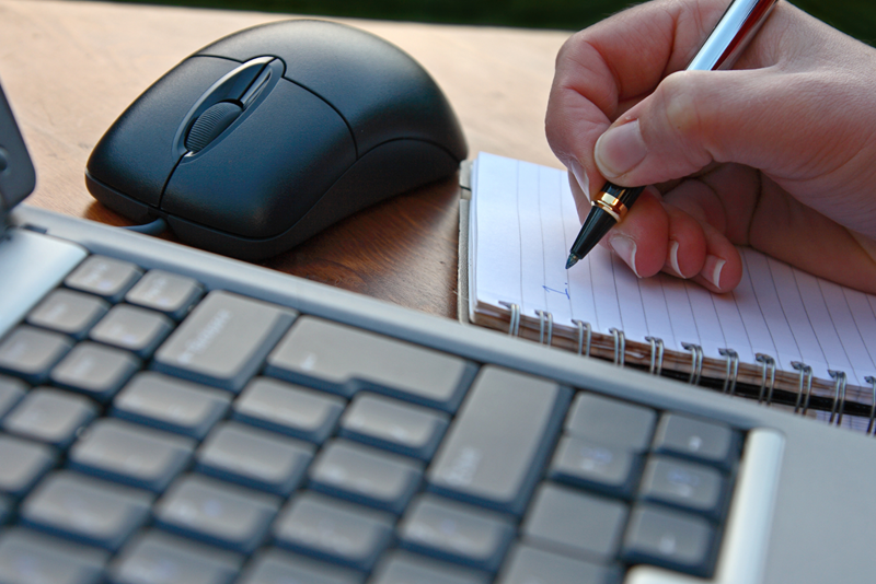 En hand håller i en penna vid sidan av en dator och en datormus 