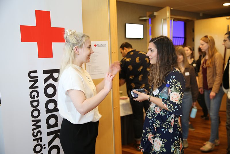 Två deltagare pratar inför en roll-up med Röda Korsets Ungdomsförbunds logga